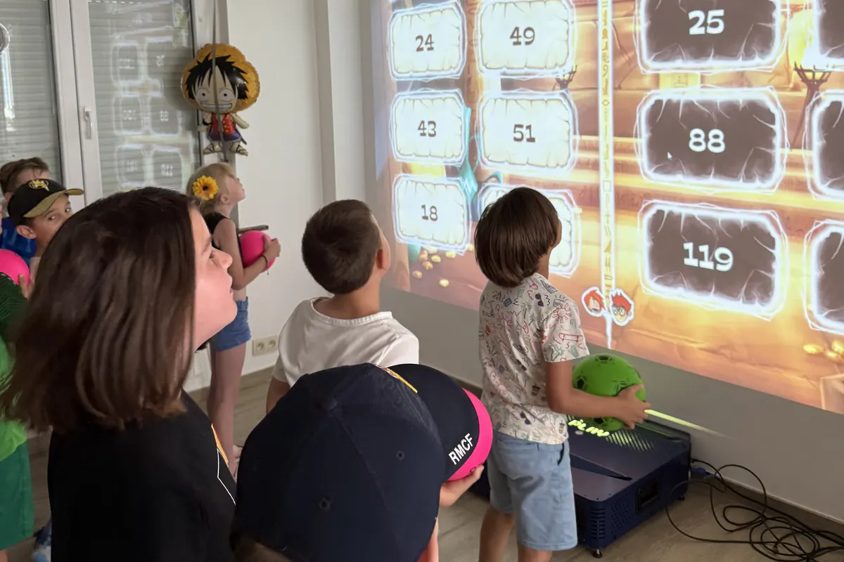 Enfants visant les bonnes réponses d'un jeu de calcul mental projeté sur le mur du salon, pendant un anniversaire à domicile