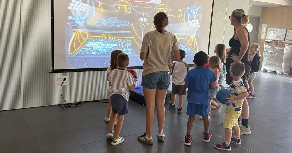 Un groupe d'enfants face à un jeu InterActis projeté sur un mur, ballon à la main