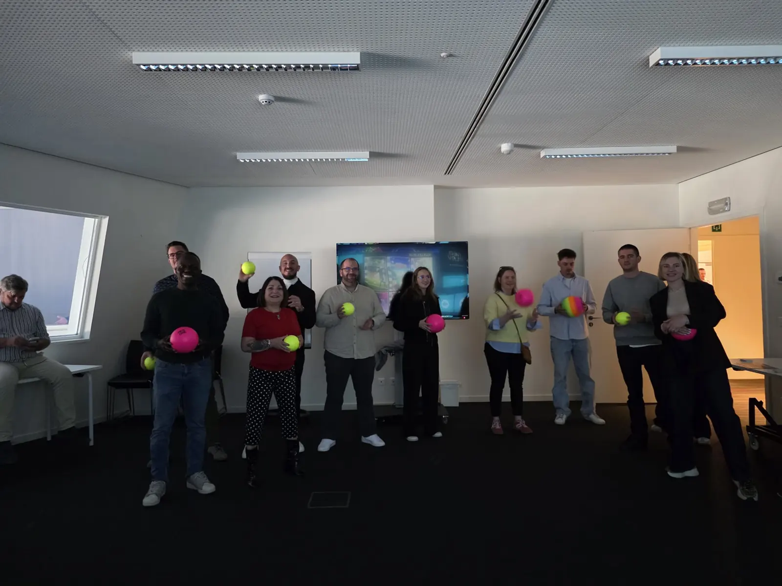 Une équipe d'une dizaine de collaborateurs debout dans leur salle de réunion, balles en main, à la fin d'une animation InterActis